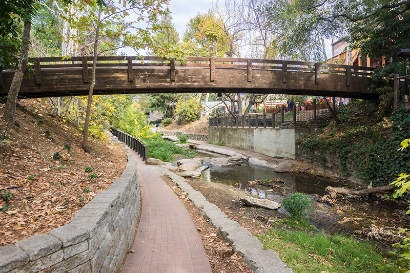 Photo of brick walkway beside creek with overhead bridge.