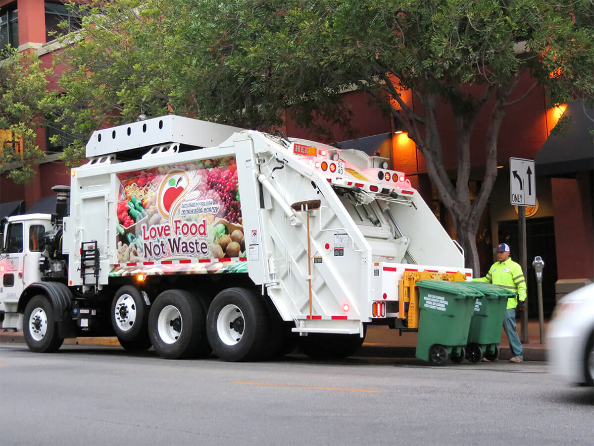 Photo of San Luis sanitation truck and worker picking up two trash carts.